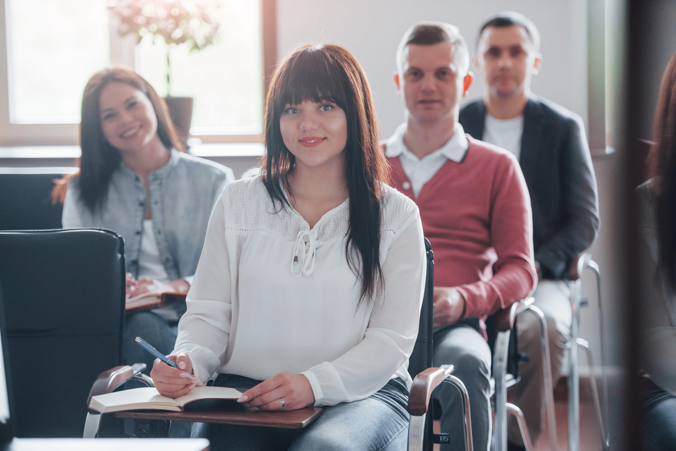 Happy brunette looks at camera. Group of people at business conference in modern classroom at daytime.