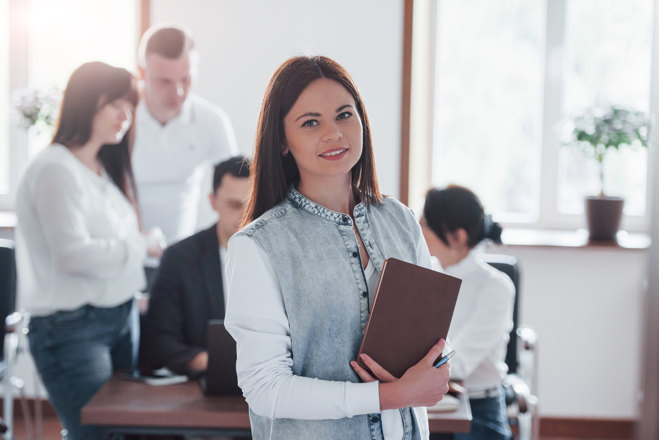 Stands in front of her colleagues. Group of people at business conference in modern classroom at daytime.